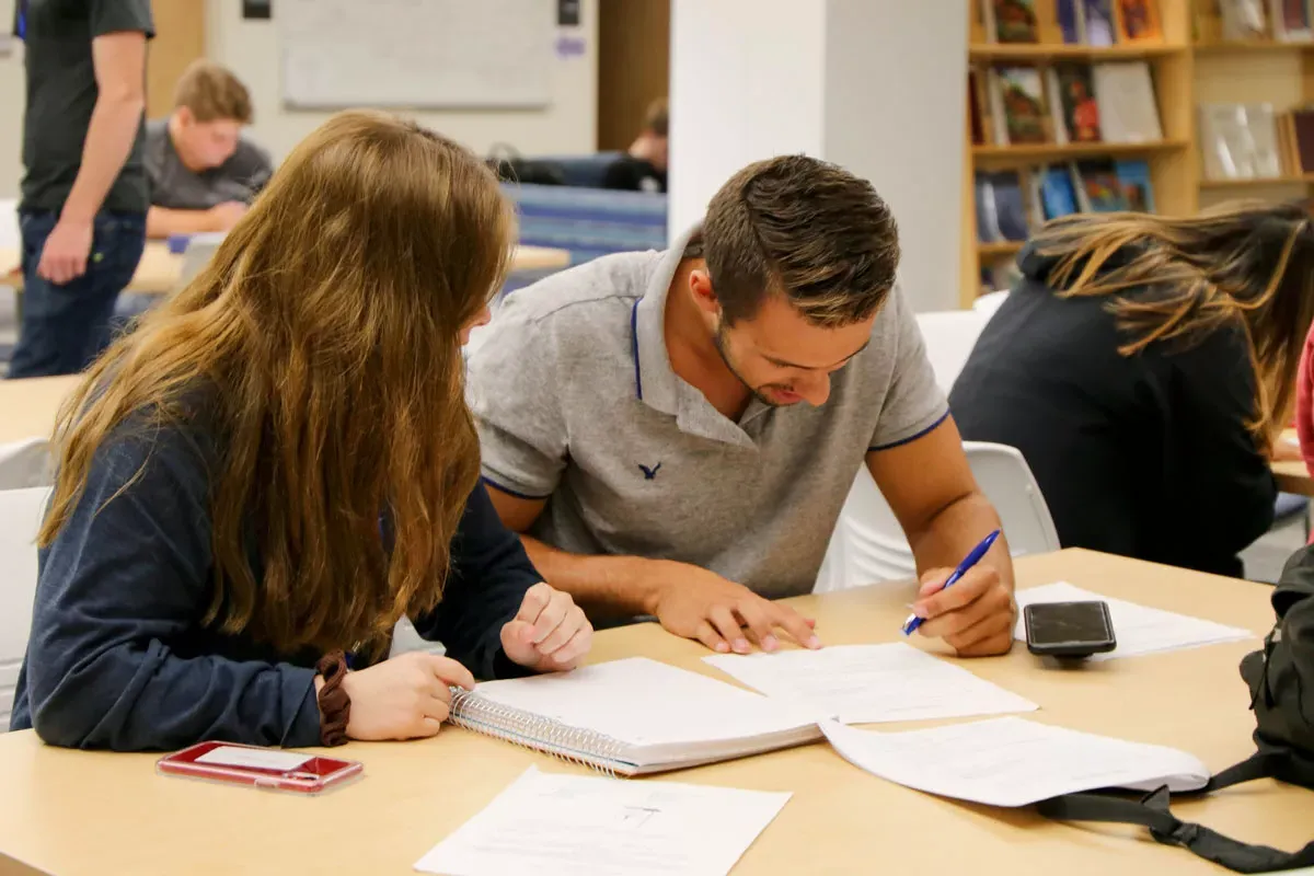 A female student tutoring a male student in a library.